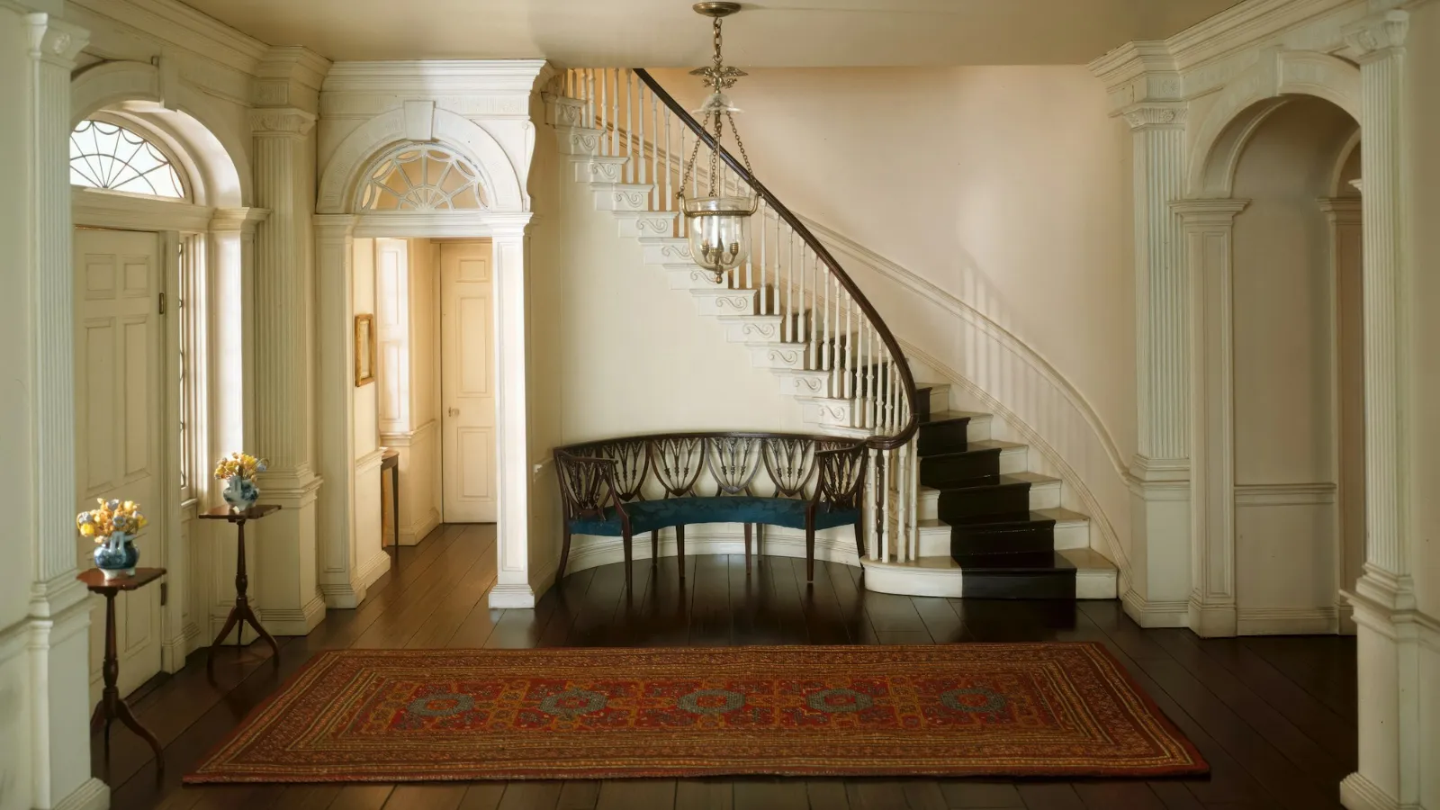 Curving staircase rising from an entrance hall with a rug