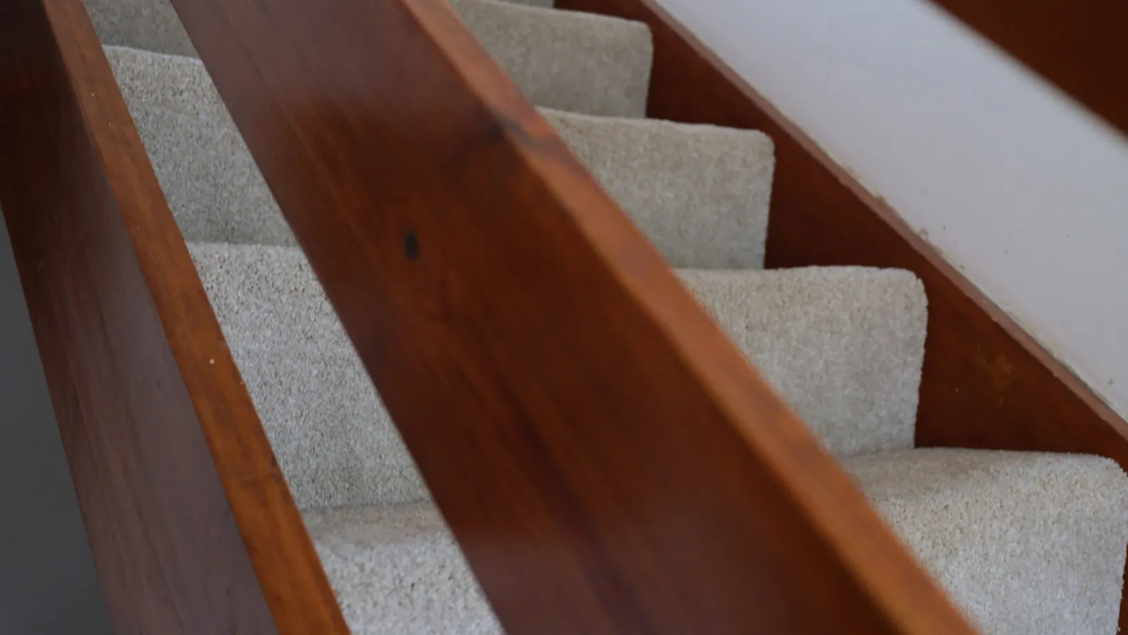 Grey carpeted stairs beside a polished wooden handrail